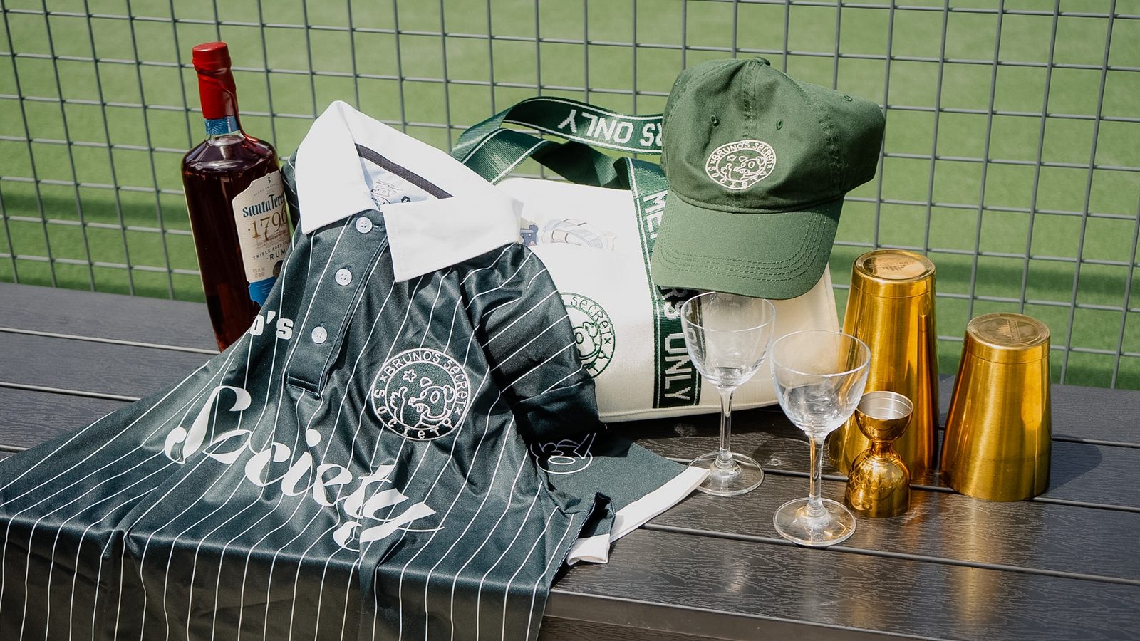 Bruno's Society flat lay — rum, gold cups, Society duffle bag